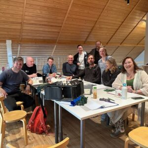 En grupp vuxna människor sitter kring ett bord och ler in i kameran.